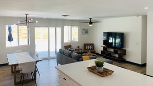 Una sala de estar moderna con un televisor de pantalla plana, un comedor con mesa y sillas, y una cocina con mostrador y armarios.