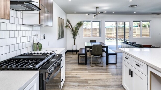 Una cocina moderna con estufa a gas, gabinetes blancos y un comedor con mesa y sillas.