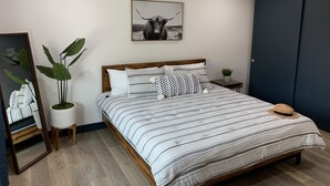 Un dormitorio con cama, ventilador de techo, un cuadro en la pared, planta en la mesita de noche y armario.