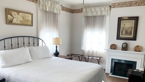 A neatly arranged bedroom with a large bed, a bedside table with a lamp, a small table, and a fireplace. - National Historic Landmark Inn (Lansing)