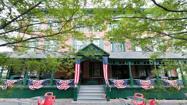 A building with green shutters, a porch with red chairs, and American flags. - National Historic Landmark Inn (Lansing)