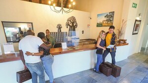 A reception area with a wooden counter, a chandelier, and a painting of a tree. - Umbhaba Lodge (Mbombela)