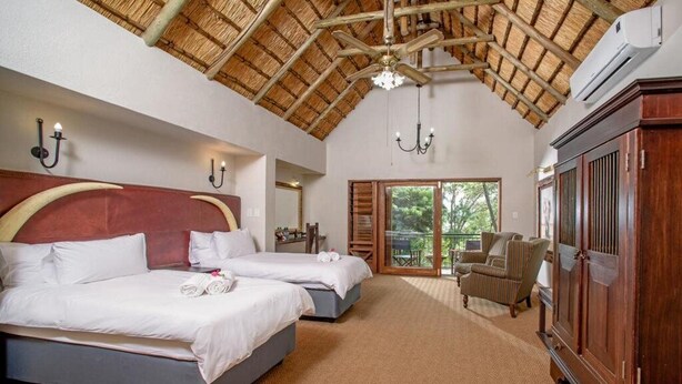 A hotel room with two beds, a wooden ceiling, a large wardrobe, and a view of the outdoors. - Umbhaba Lodge (Mbombela)