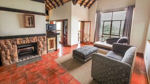 A spacious living room with a fireplace, a sofa, and a television. - Umbhaba Lodge (Mbombela)