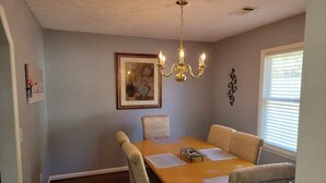 A dining room with a wooden table, six chairs, a chandelier, framed artwork, and a window with blinds. - Near Ft. Moore - Ft. Benning 4 br 2 bath renovated charming home  (Columbus)