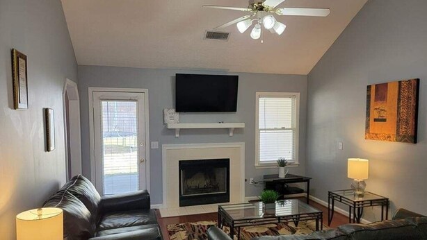 A living room with a fireplace, a flat-screen TV, a ceiling fan, and a sofa. - Near Ft. Moore - Ft. Benning 4 br 2 bath renovated charming home  (Columbus)