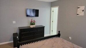 A bedroom with a bed, a dresser, a television on the wall, and a door. - Near Ft. Moore - Ft. Benning 4 br 2 bath renovated charming home  (Columbus)
