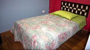 Una cama individual con una colcha estampada y una almohada verde en una habitación con paredes azules y rojas.