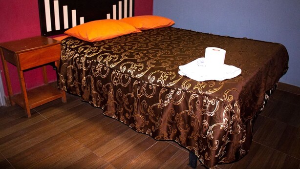 Una cama bien hecha con una colcha estampada, dos almohadas naranjas y un sombrero blanco sobre la cama.