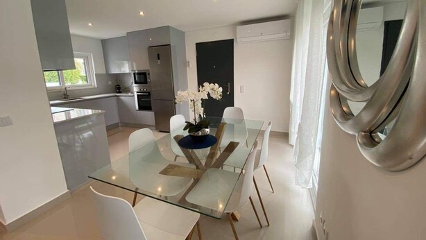 Una cocina moderna con electrodomésticos de acero inoxidable, una mesa de comedor de vidrio con sillas blancas y un centro de mesa decorativo con orquídeas.
