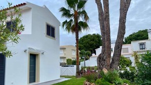 Un edificio moderno blanco con un pequeño jardín, palmeras y una valla blanca.