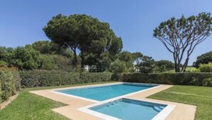 Una piscina rectangular con borde de azulejos, rodeada por un césped cuidado y setos.