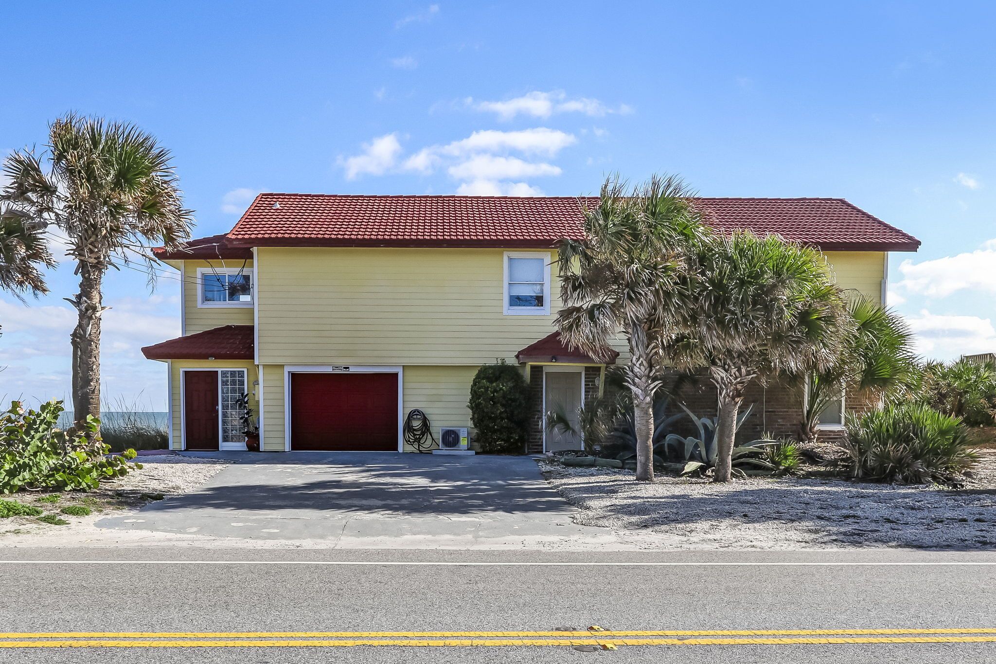 A two-story yellow house with a red roof, a red garage door, and a small front porch.