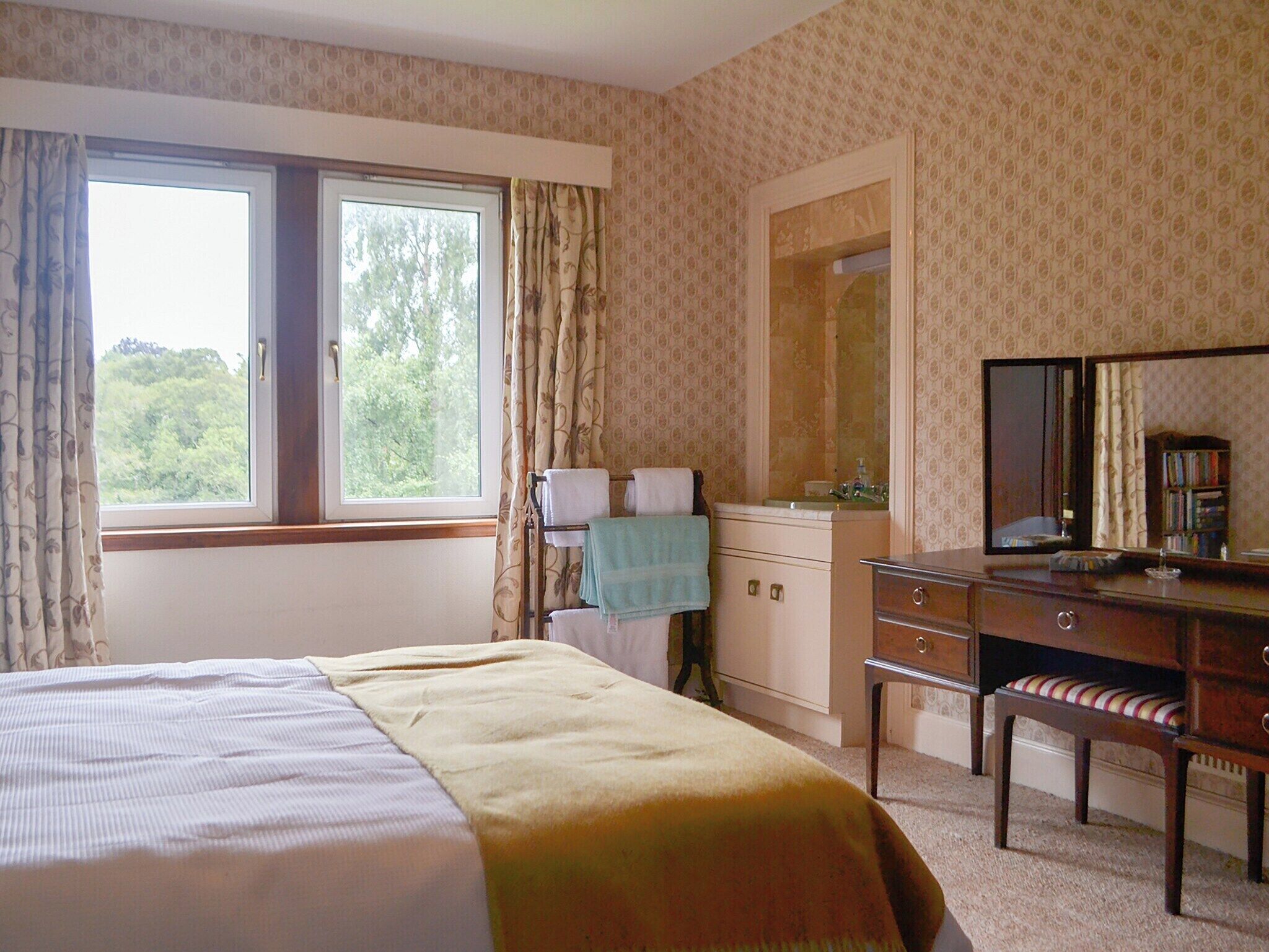 Een slaapkamer met een groot bed, een dressoir, een spiegel en een raam met gordijnen.