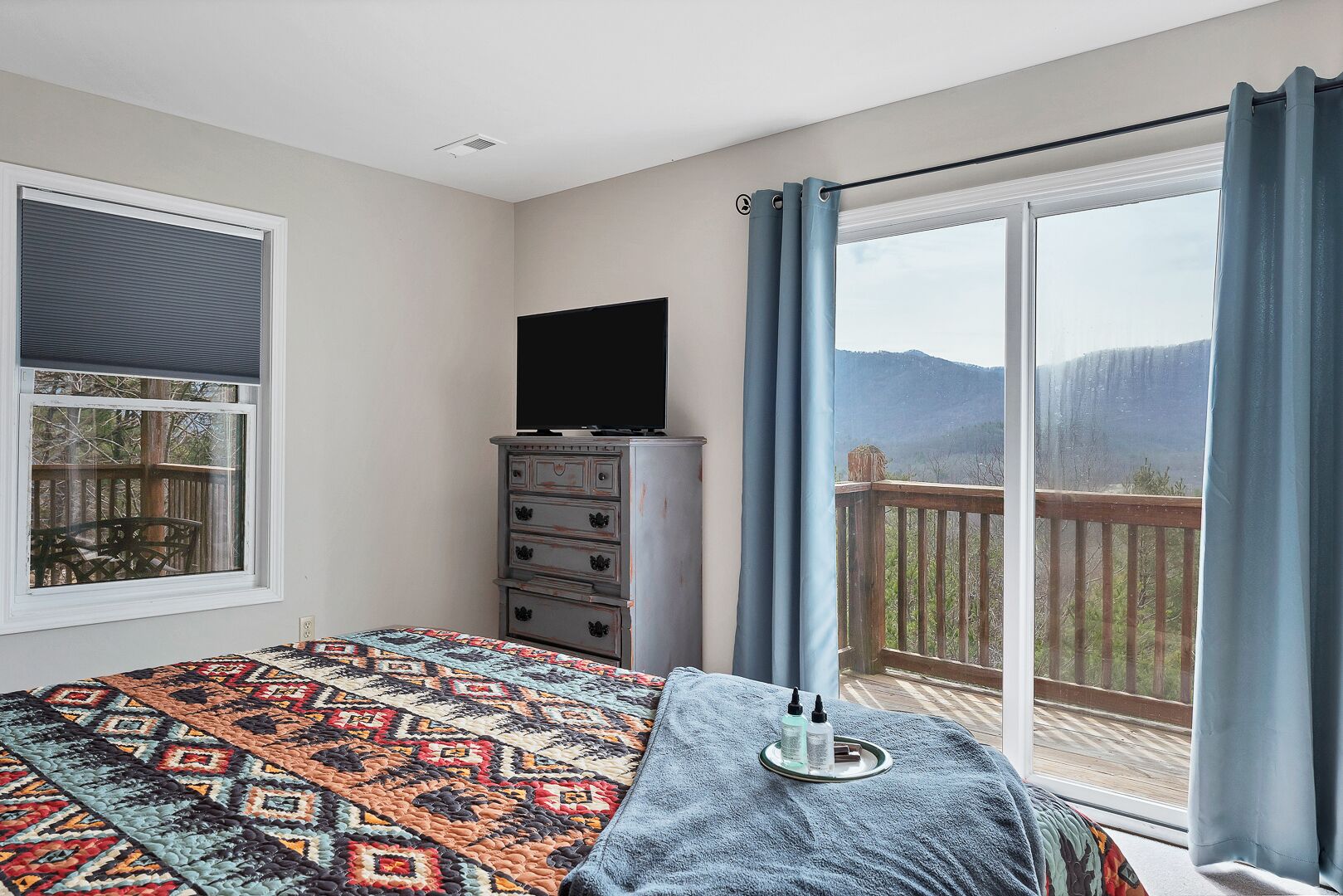 A bedroom with a bed, dresser, TV, and a balcony with a view.
