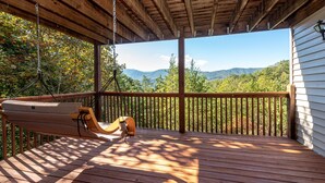 Una terraza de madera con una silla hamaca con vistas a un paisaje montañoso.