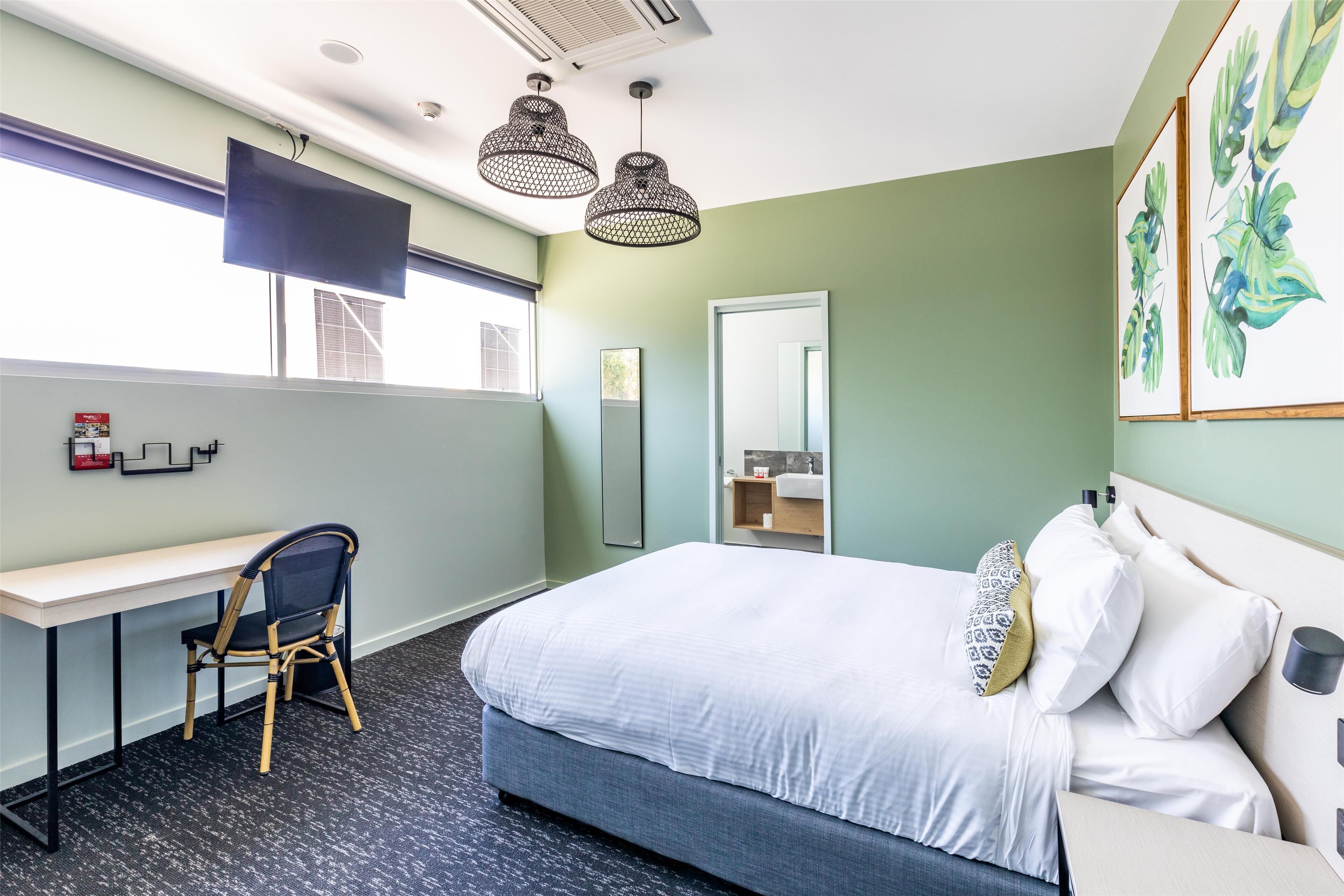 A hotel room with a bed, desk, chair, and artwork on the walls.