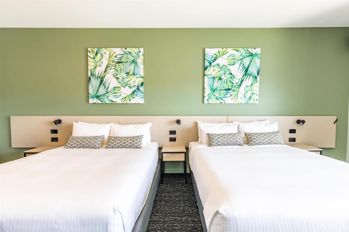 A hotel room with two beds, a headboard, bedside tables, and wall art.