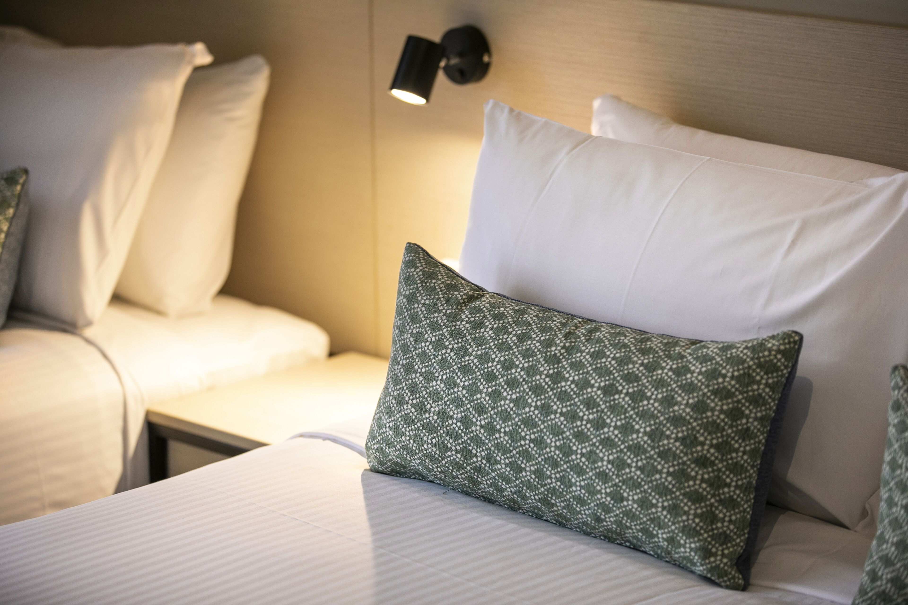 Una cama bien hecha con sábanas blancas y un cojín estampado en verde.