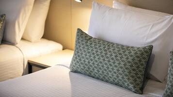 Una cama bien hecha con sábanas blancas y un cojín estampado en verde.