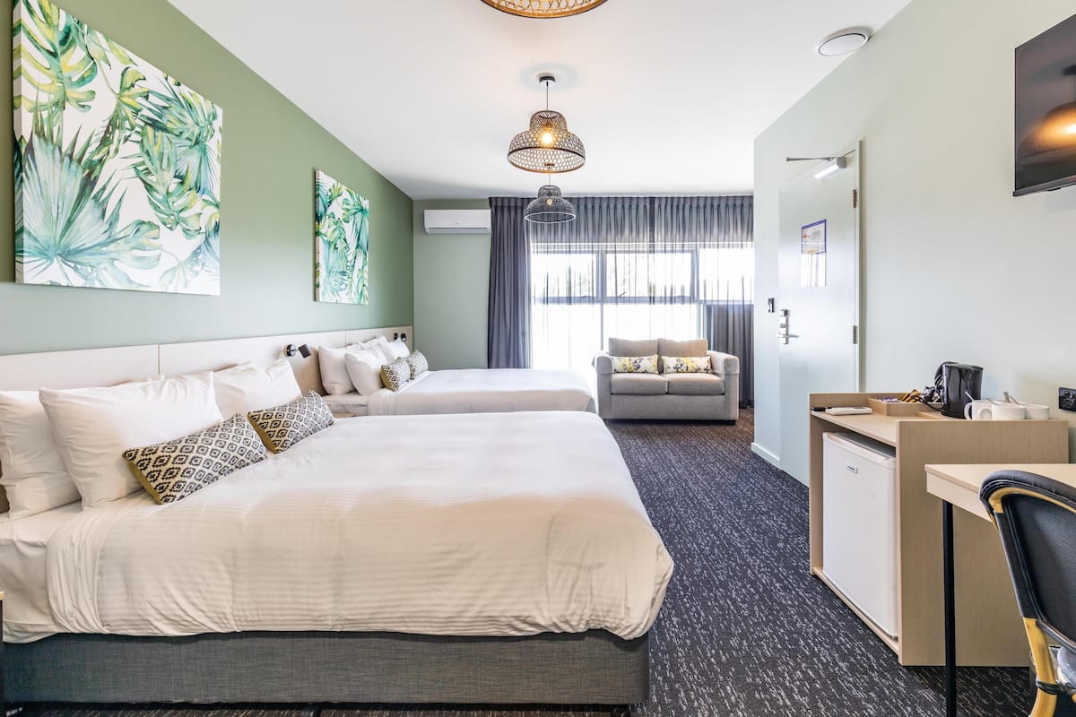 A hotel room with two beds, a desk, a chair, and a large window.