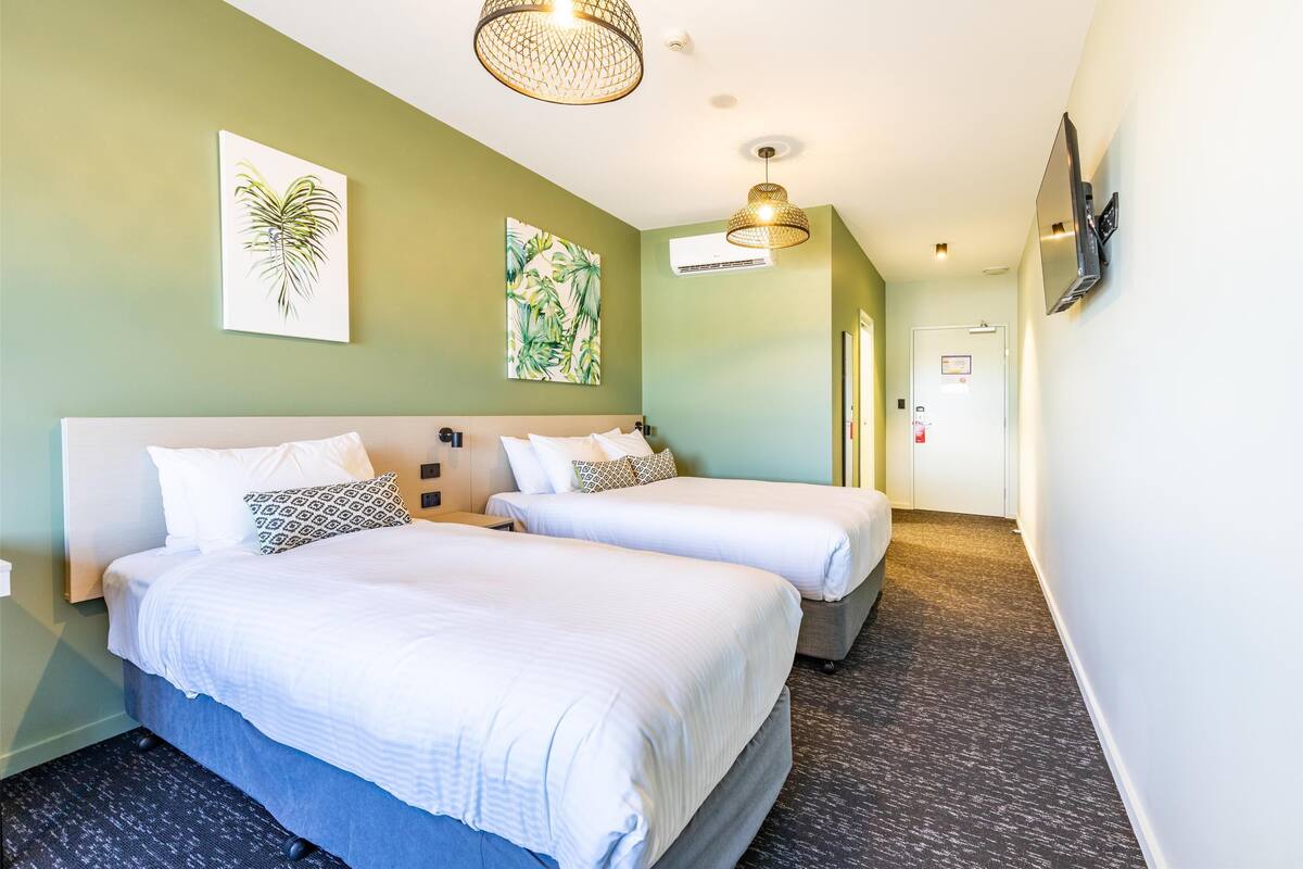A hotel room with two beds, a flat-screen TV mounted on the wall, and artwork on the walls.