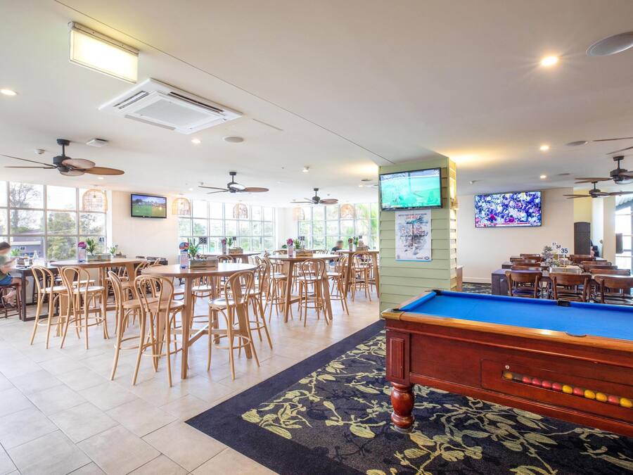A spacious indoor area with multiple tables and chairs, a pool table, ceiling fans, and large windows allowing natural light.