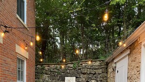 Un patio al aire libre con un muro de piedra, un edificio de ladrillo y luces colgantes.
