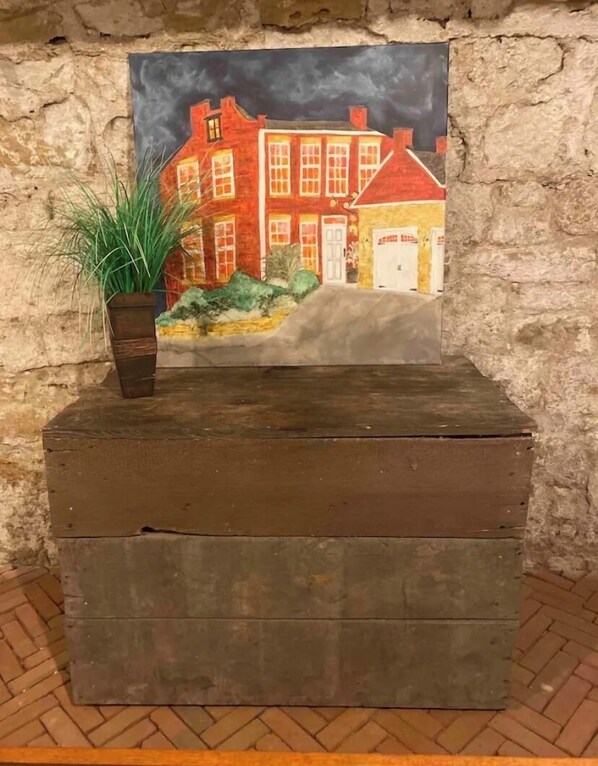 Una pintura de un edificio rojo con una puerta blanca, colocada sobre una caja de madera frente a un muro de piedra.