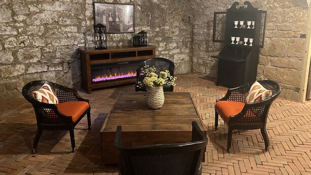 Una habitación acogedora con pared de piedra, chimenea, dos sillones de mimbre con cojines, una mesa de centro de madera y un jarrón decorativo.