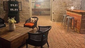 Un ambiente acogedor con pared de piedra, una mesa de madera, sillas de mimbre y una zona de bar.