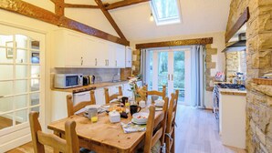 Una cocina acogedora con vigas de madera, una mesa de comedor preparada para cuatro personas y vistas al jardín a través de la ventana.