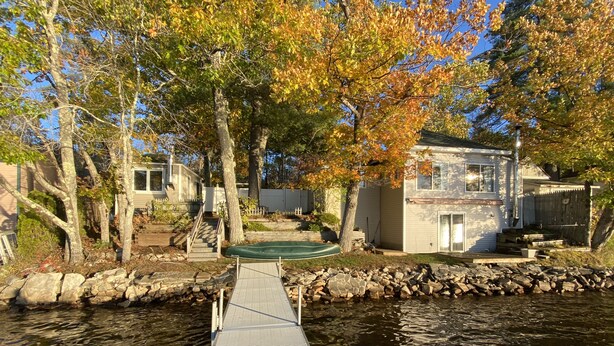 A riverside dock leading to a house with a stone wall and a wooden deck.