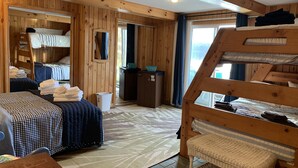 A wooden cabin room with bunk beds, a desk, and a small kitchenette.