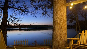 A lakeside seating area with a fire pit, wooden chairs, and a view of the lake at dusk.