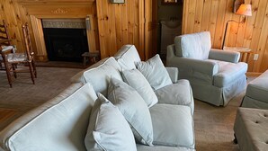 A living room with a light grey sofa set, a wooden wall, a fireplace, and a lamp.