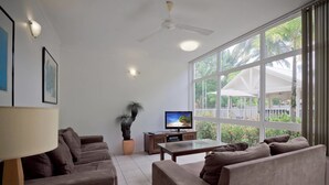 A spacious living room with a large window, a ceiling fan, a television, and a potted plant.