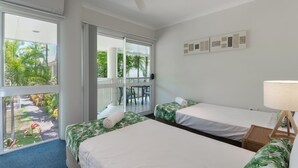 A hotel room with two beds, a balcony, and a view of greenery.