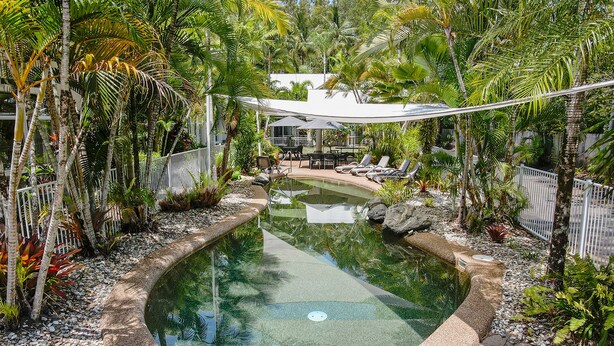 Une piscine circulaire entourée de plantes tropicales et délimitée par une clôture blanche.