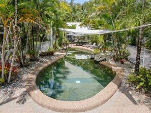 Une piscine circulaire entourée de plantes tropicales et délimitée par une clôture blanche.