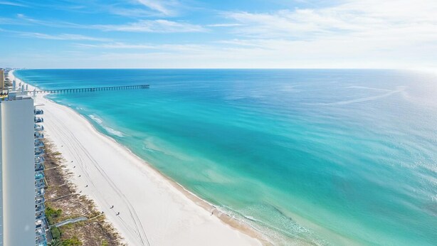 Une plage avec une jetée qui s’avance dans l’océan, un ciel dégagé et une rive de sable blanc.