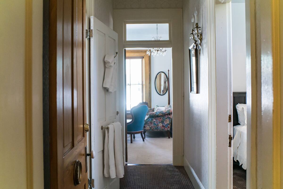 A hallway leading to a bedroom with a bed, a chair, and a mirror on the wall.