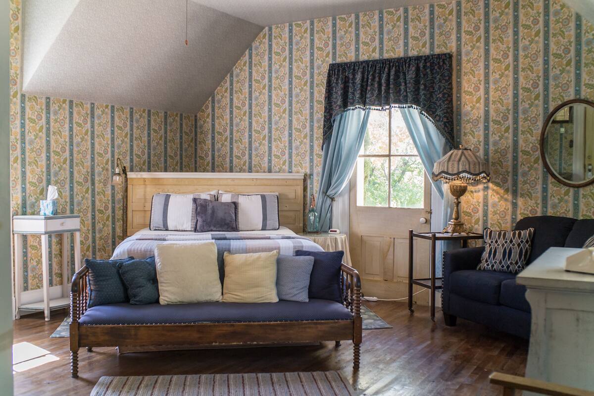 A bedroom with a wooden bed, a blue sofa, a small table, and a lamp.