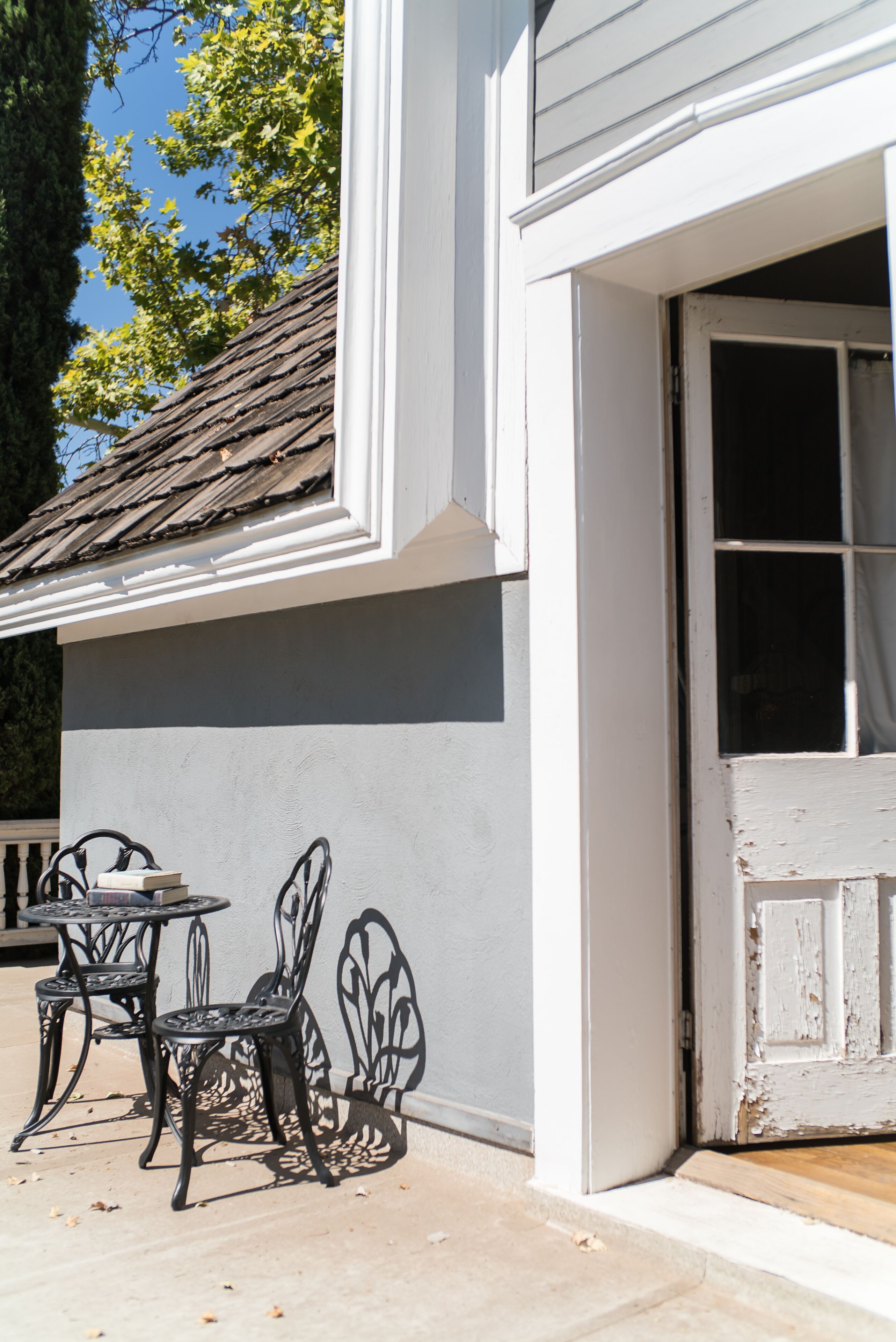 A building exterior with a white door, a window, and a small outdoor seating area with metal chairs and a table.