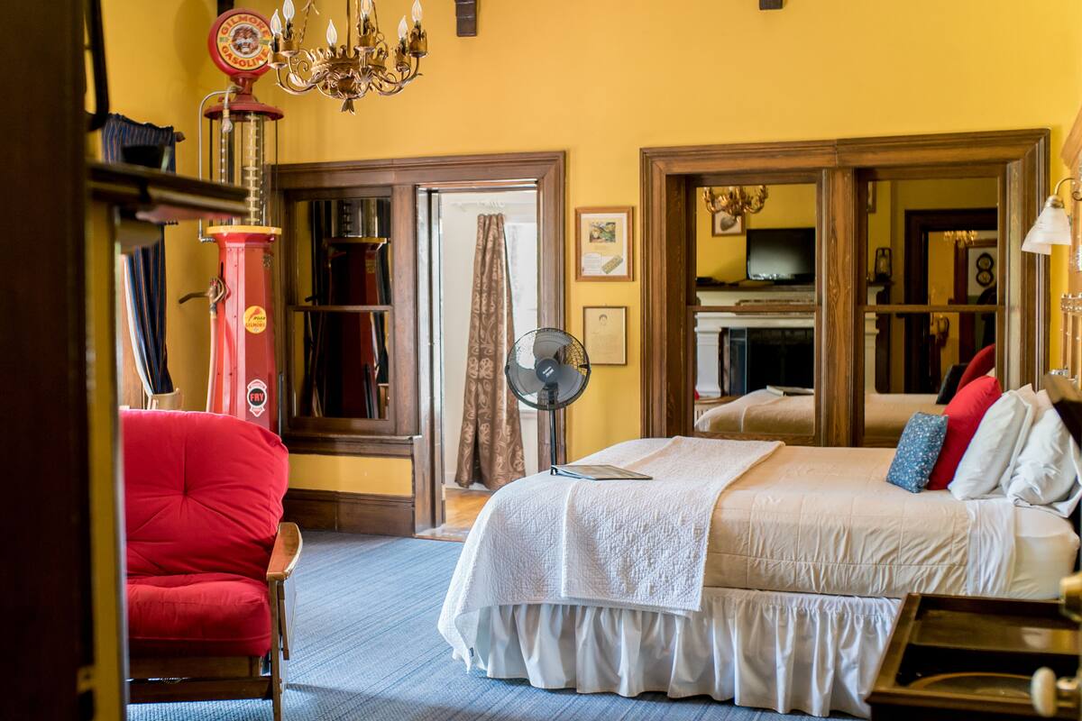 A bedroom with a large bed, a red armchair, a fan, and a chandelier.