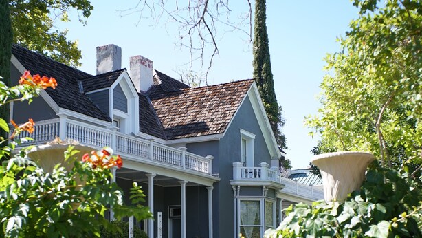 Een tweelaags huis met een veranda, schoorsteen en een verzorgd gazon.