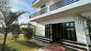 Un edificio moderno de dos pisos con un balcón, ventanas grandes y un área de entrada pavimentada.