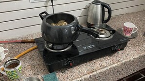 Una cocina con estufa a gas, hervidor, cafetera y una taza sobre la encimera.