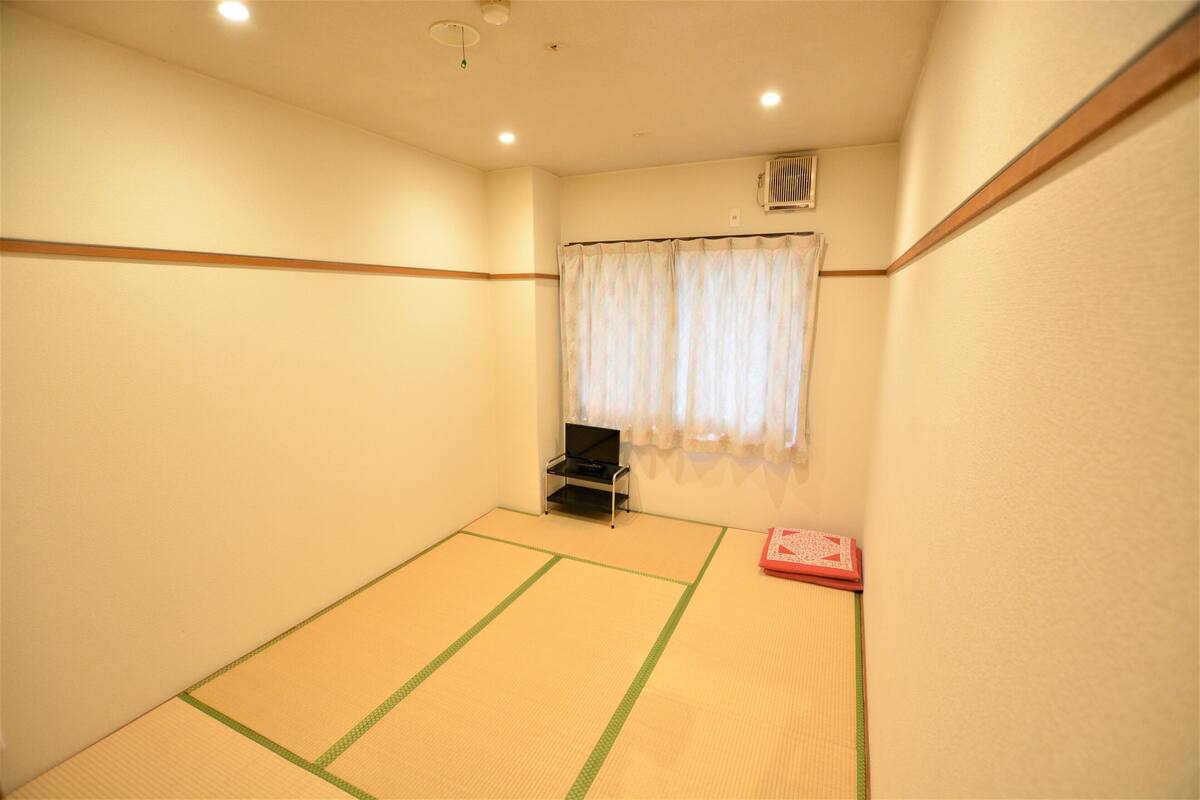 A tatami mat room with a futon bed, a small table, and a window with curtains.
