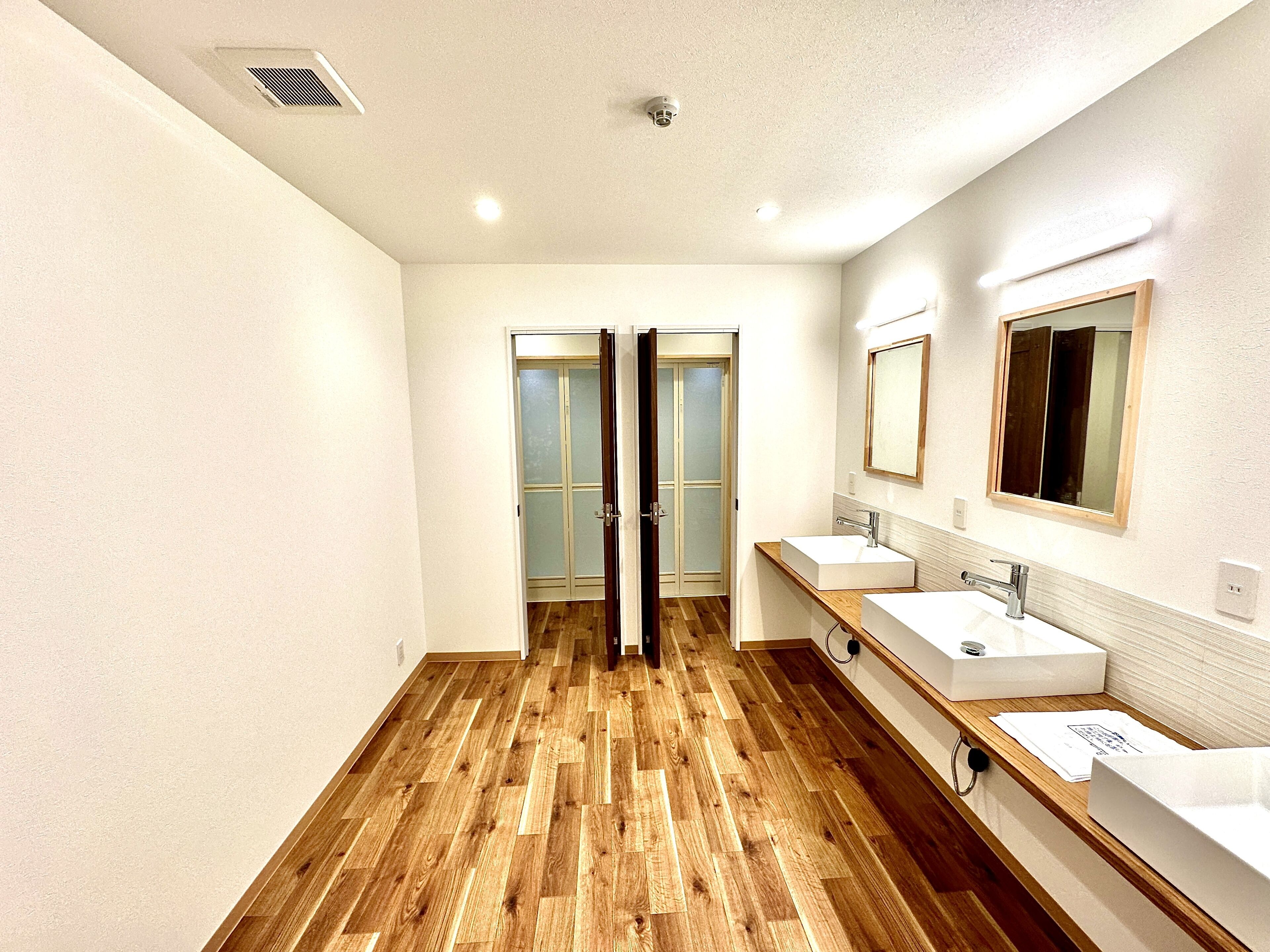 Un baño moderno con suelo de madera, dos lavamanos y una puerta de vidrio que da a la zona de ducha.